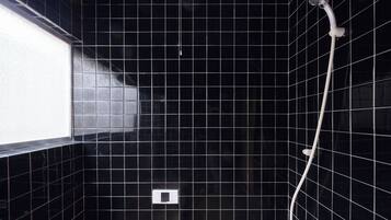 A bathroom with black tiled walls, a window on the left, and a shower with a handheld showerhead.