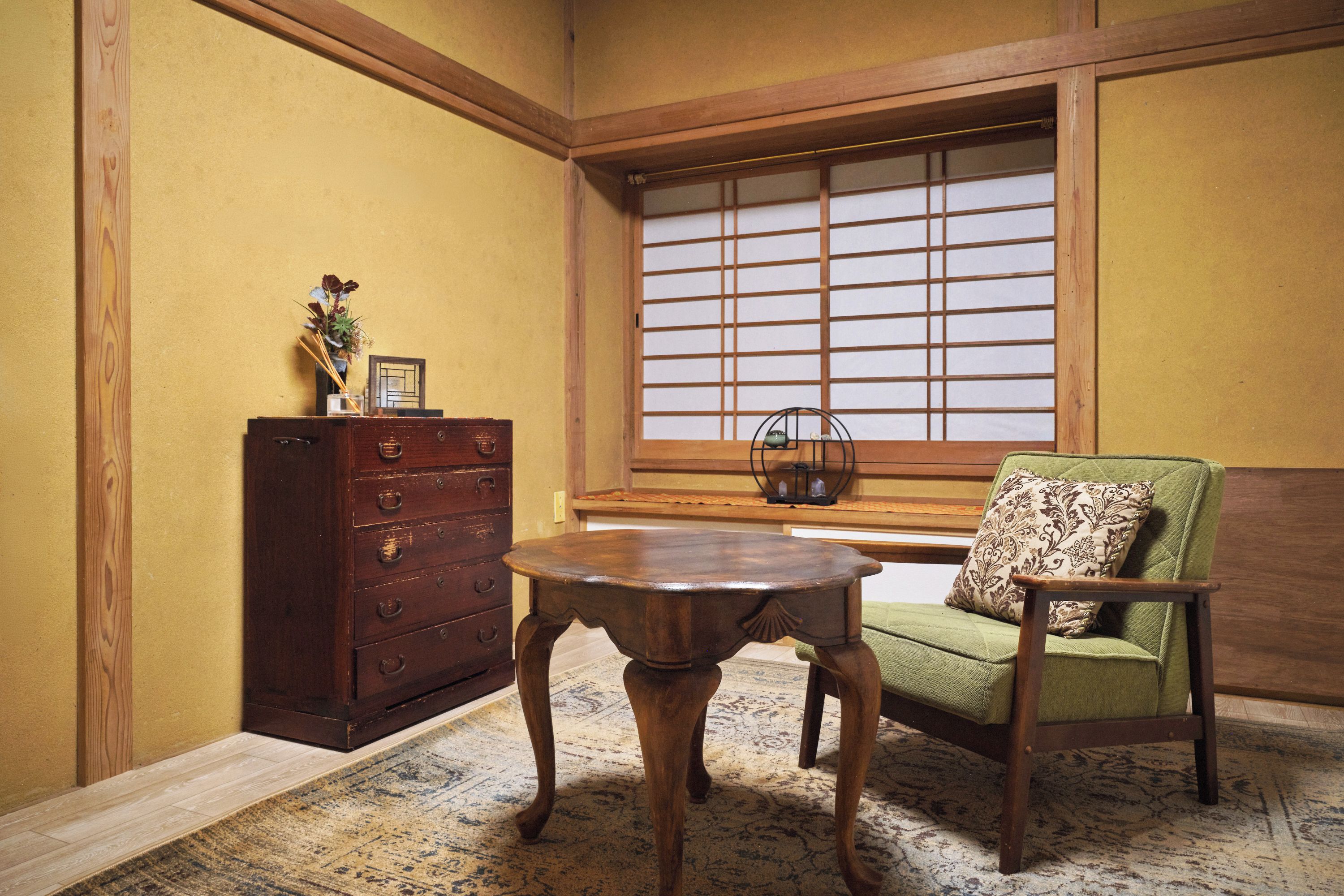 Ein traditioneller japanischer Raum mit Tatami-Böden, einem Holztisch, einem grünen Stuhl und einem Holzschrank.