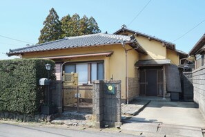A traditional Japanese house with a tiled roof, a wooden gate, and a stone wall.