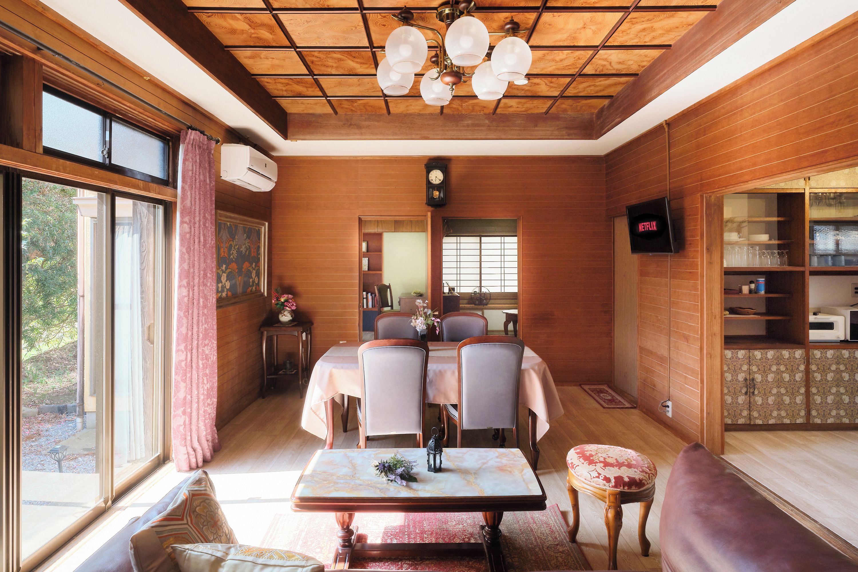 A dining area with a wooden ceiling, a table with chairs, a clock, and a television displaying 'NETFLIX'.