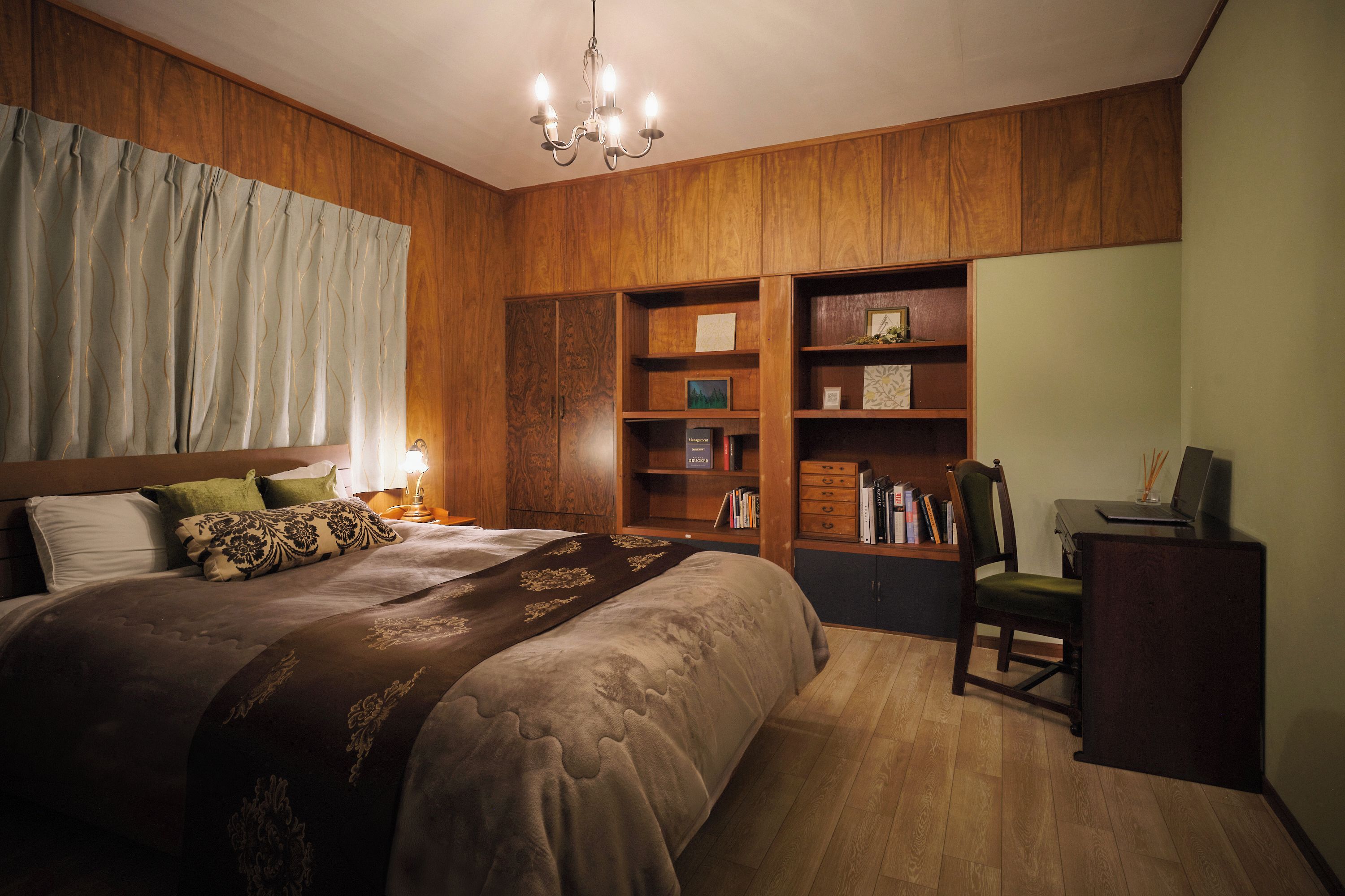 A bedroom with a large bed, wooden paneling, a desk with a chair, and a bookshelf.