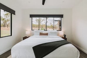 A bedroom with a large bed, two bedside tables with lamps, a window with a view of trees, and a black headboard.