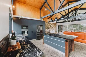 Cozinha moderna com parede de pedra, forno embutido e área de jantar com banco.