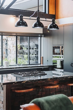 A modern kitchen with a large island, bar stools, a gas stove, and pendant lighting.