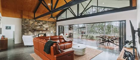 A spacious living area with a leather sofa, a stone fireplace, and a large glass door leading to an outdoor patio.