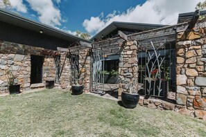 A stone house with a covered patio area, potted plants, and a clear sky. - The Riverstone | Luxury Bush Retreat (Millstream)
