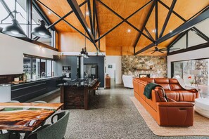 A spacious living area with a large wooden ceiling, a stone fireplace, and a leather sofa. - The Riverstone | Luxury Bush Retreat (Millstream)