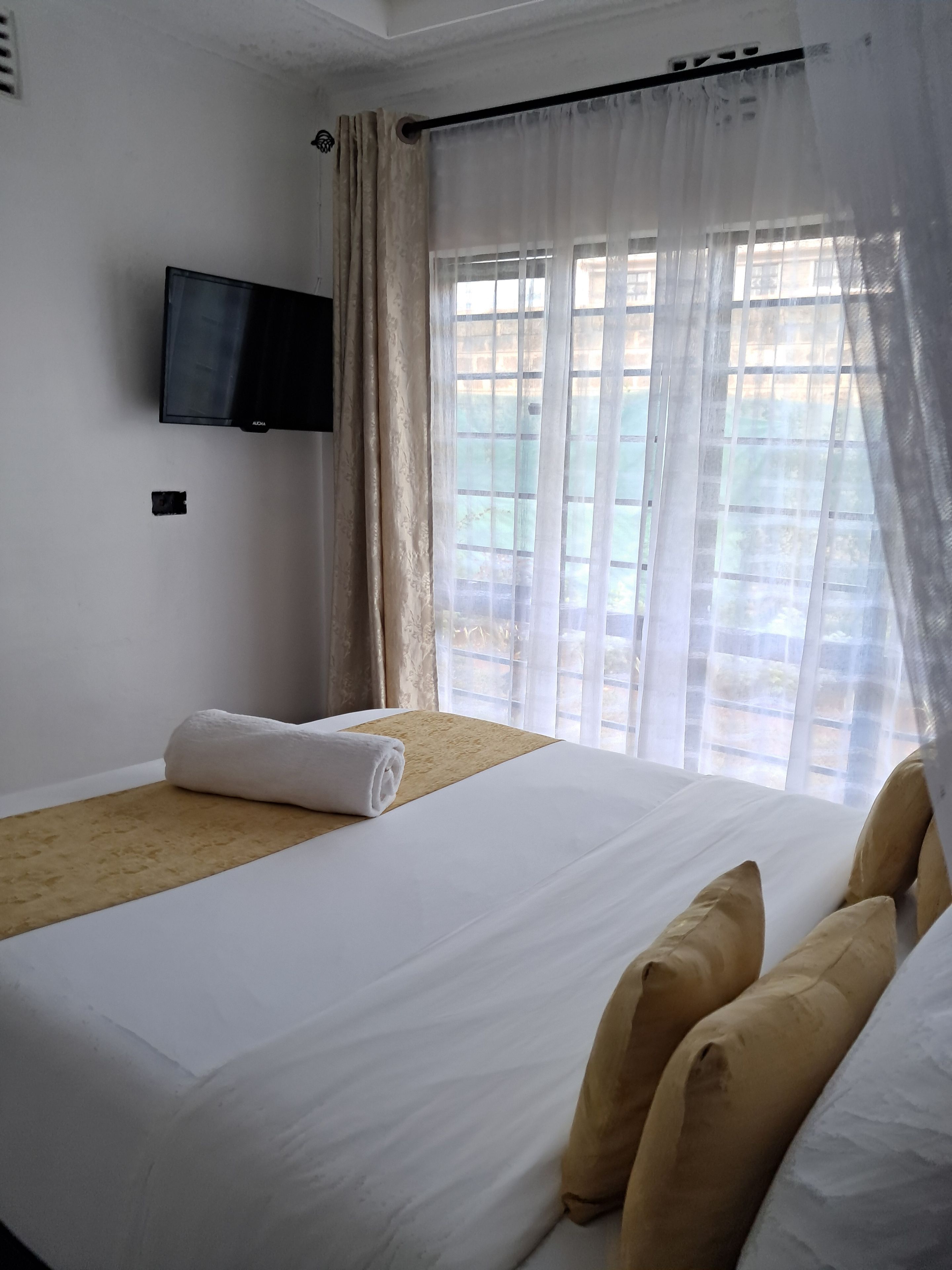 Ein Hotelzimmer mit einem Bett, einem an der Wand befestigten Fernseher und einem Fenster mit Vorhängen.