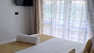 Ein Hotelzimmer mit einem Bett, einem an der Wand befestigten Fernseher und einem Fenster mit Vorhängen.