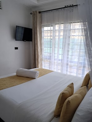 Une chambre d’hôtel avec un lit, un téléviseur fixé au mur et une fenêtre avec des rideaux.