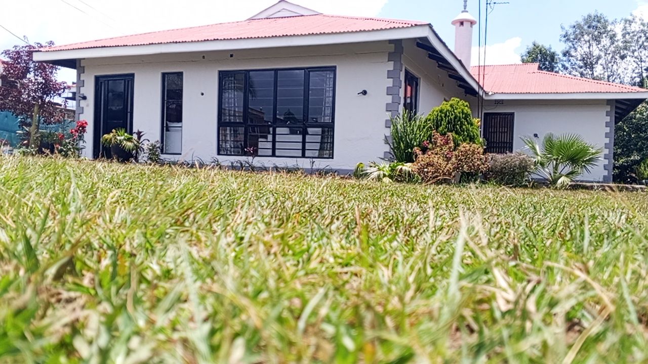 Ein eingeschossiges Haus mit rotem Dach, einer Veranda und einem kleinen Garten.