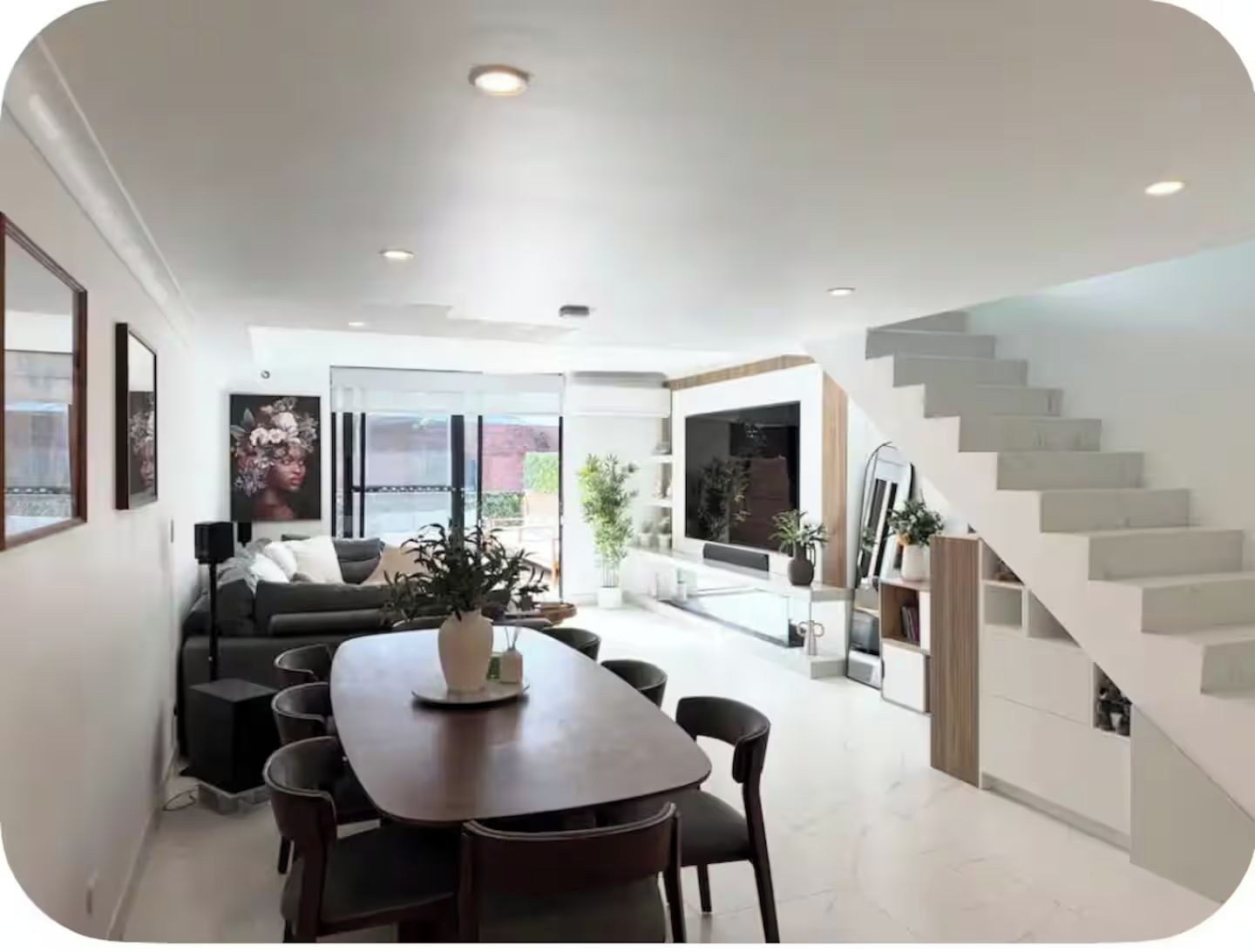 A modern interior with a dining area, sofa, staircase, and large windows.