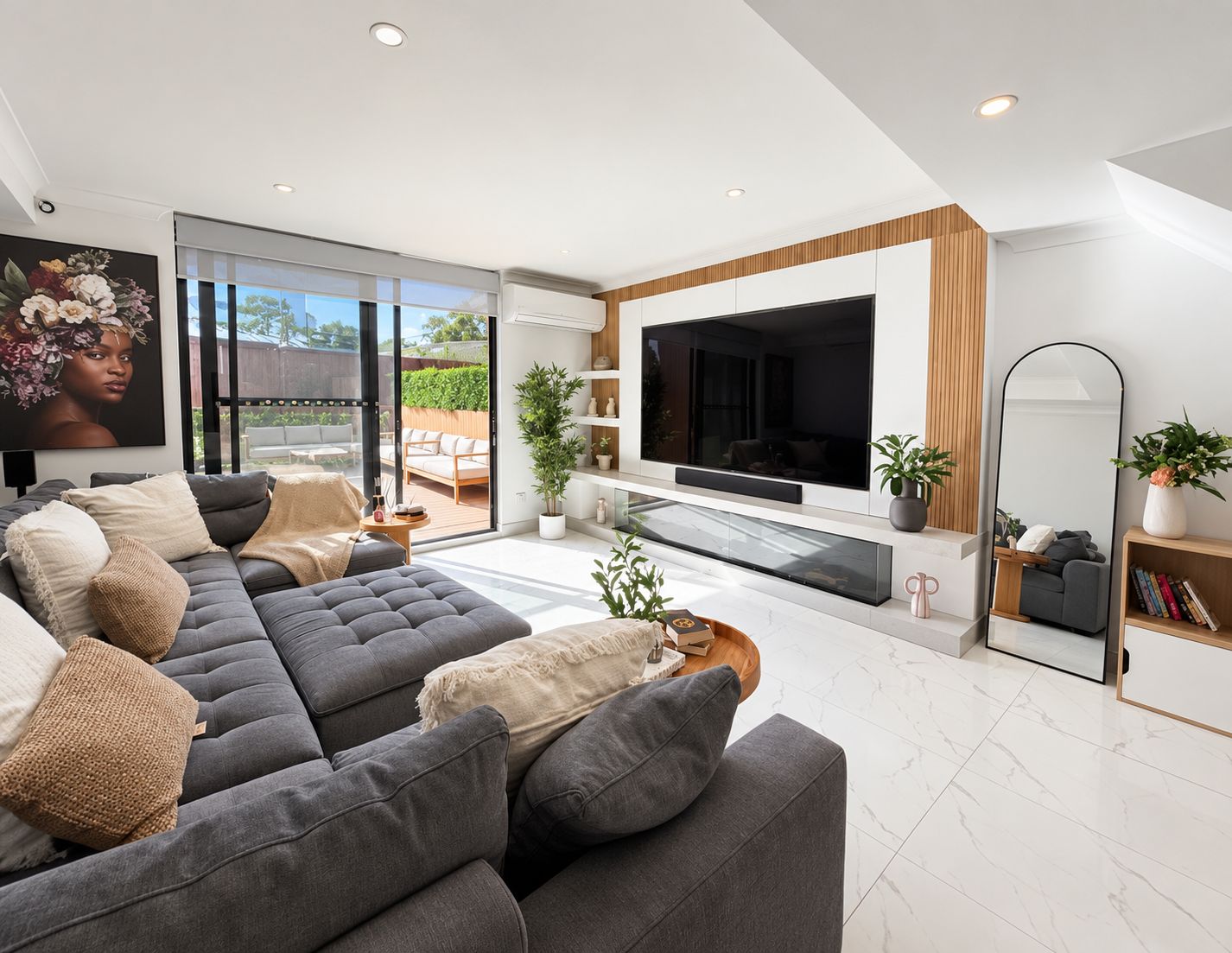 Una sala de estar moderna con un sofá seccional grisáceo, un televisor de pantalla plana y un ventanal con vistas a un jardín.
