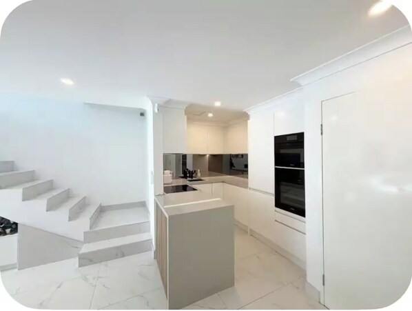 A modern kitchen with a central island, built-in appliances, and a staircase leading to another level.