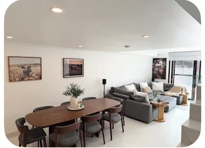 A modern living room with a dining area, featuring a sofa set, a dining table with chairs, and two wall-mounted paintings.