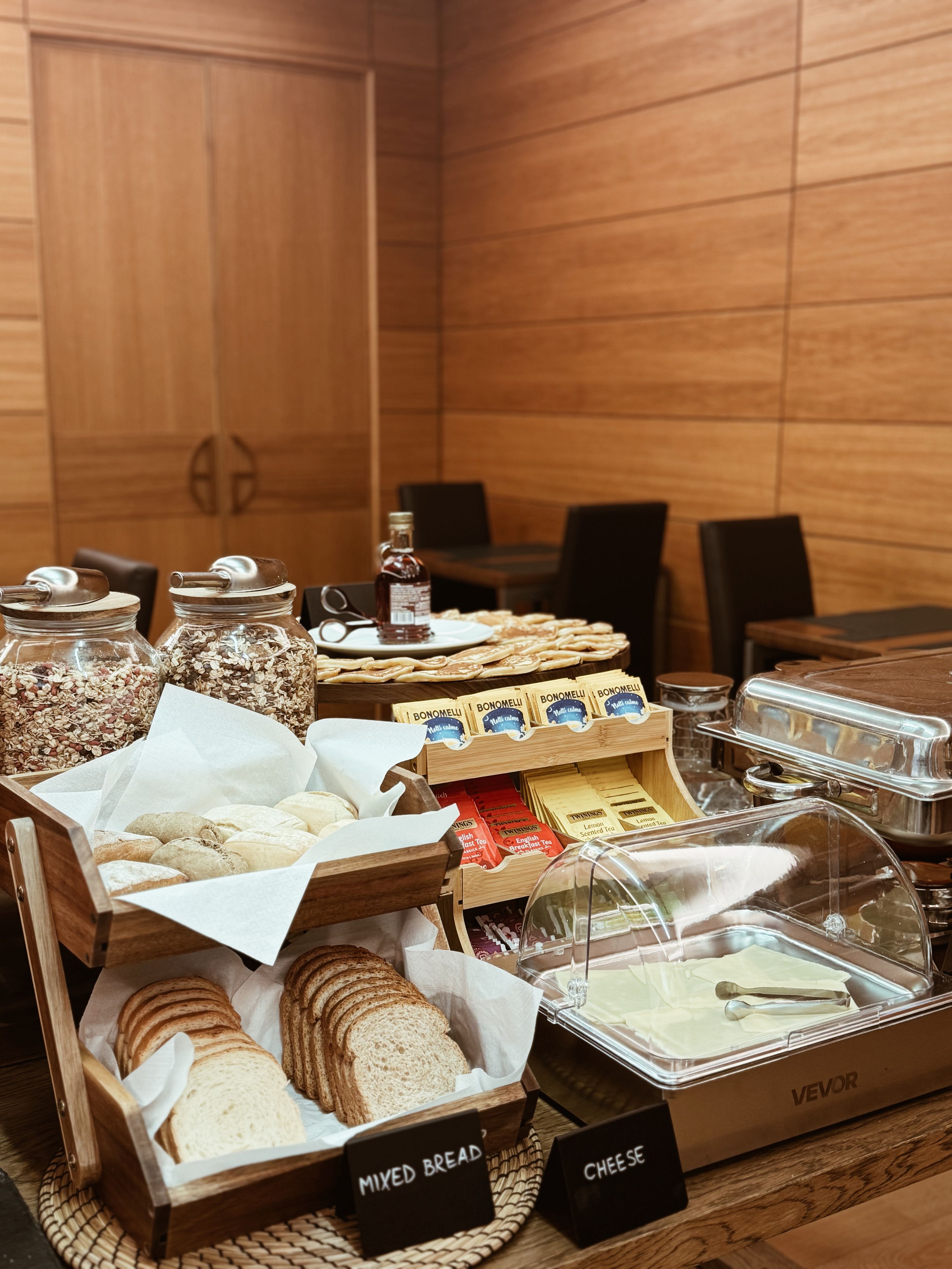 A buffet with labeled containers of mixed bread, cheese, and various spreads.