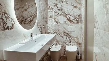 Un baño moderno con un espejo ovalado grande, un lavamanos rectangular, un bidé y un inodoro.