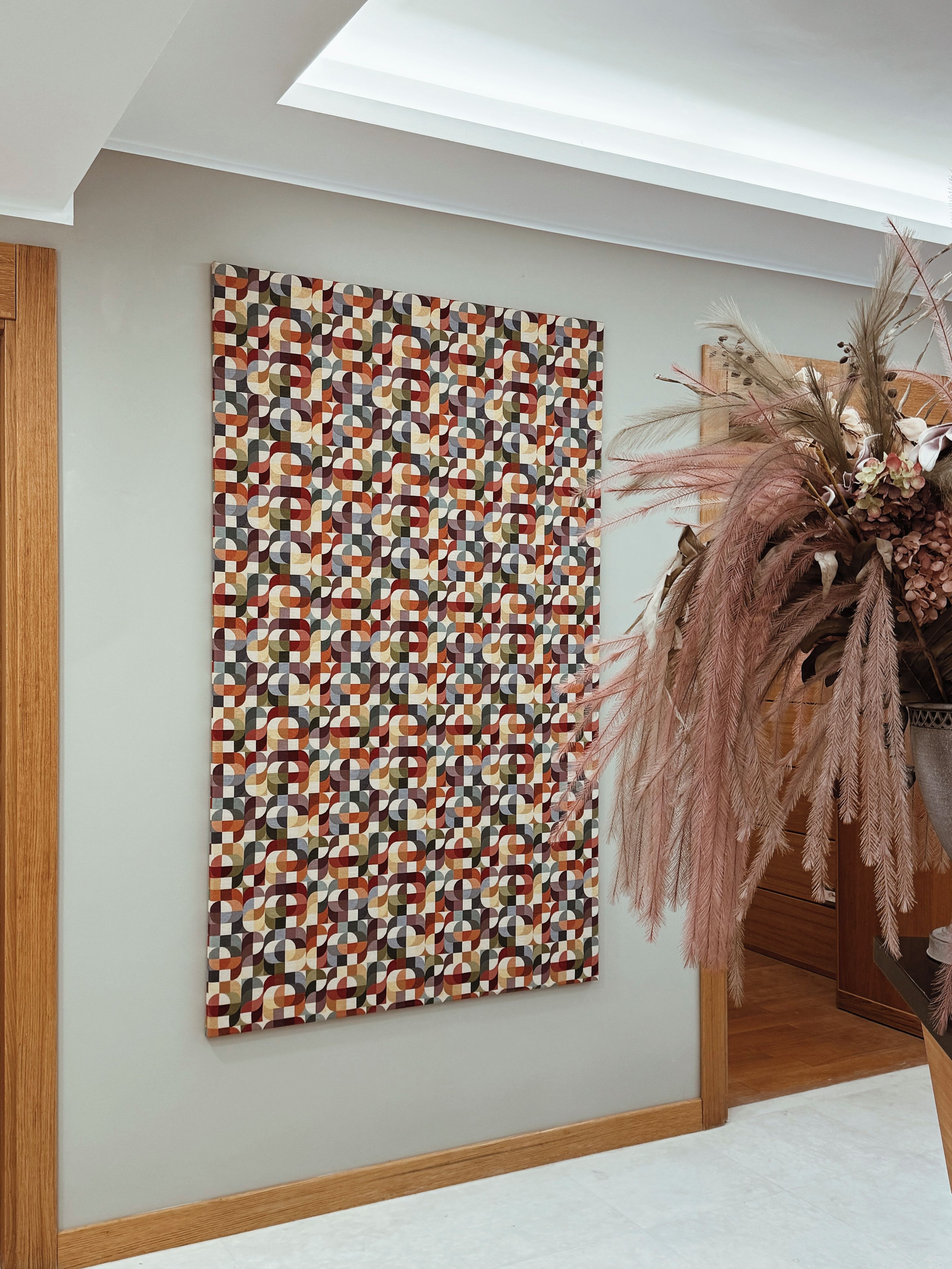 Een kamer met een kunstwerk met een geometrisch patroon aan de muur, een houten vloer en een decoratieve plantenpresentatie.