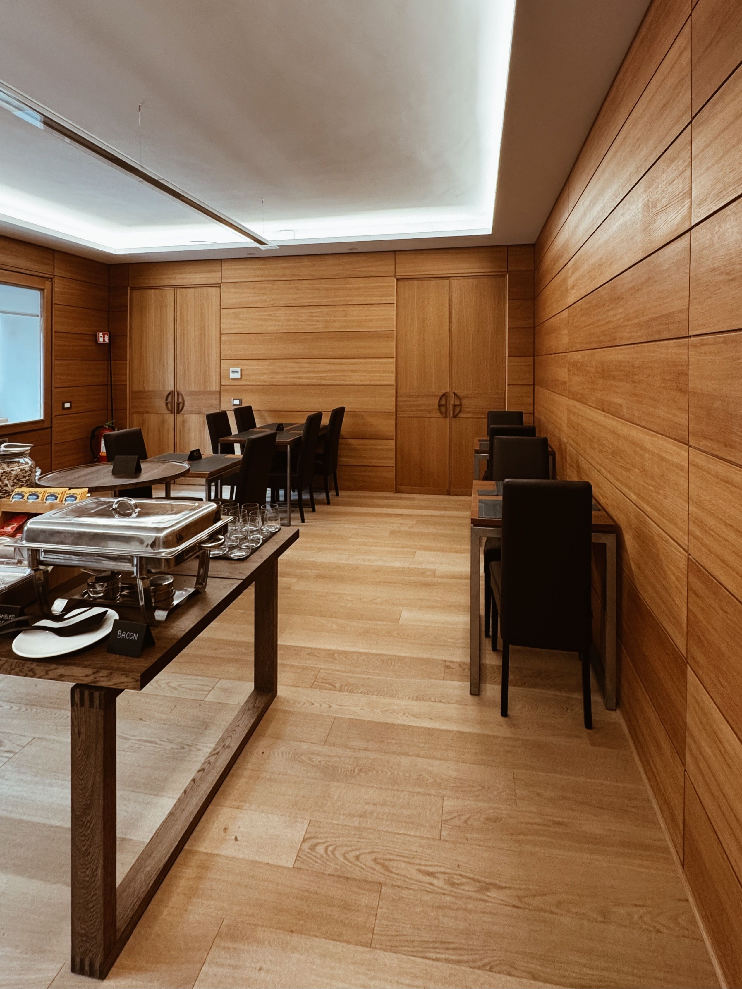 Een moderne eetruimte met houten lambrisering, een buffetopstelling en meerdere eettafels.
