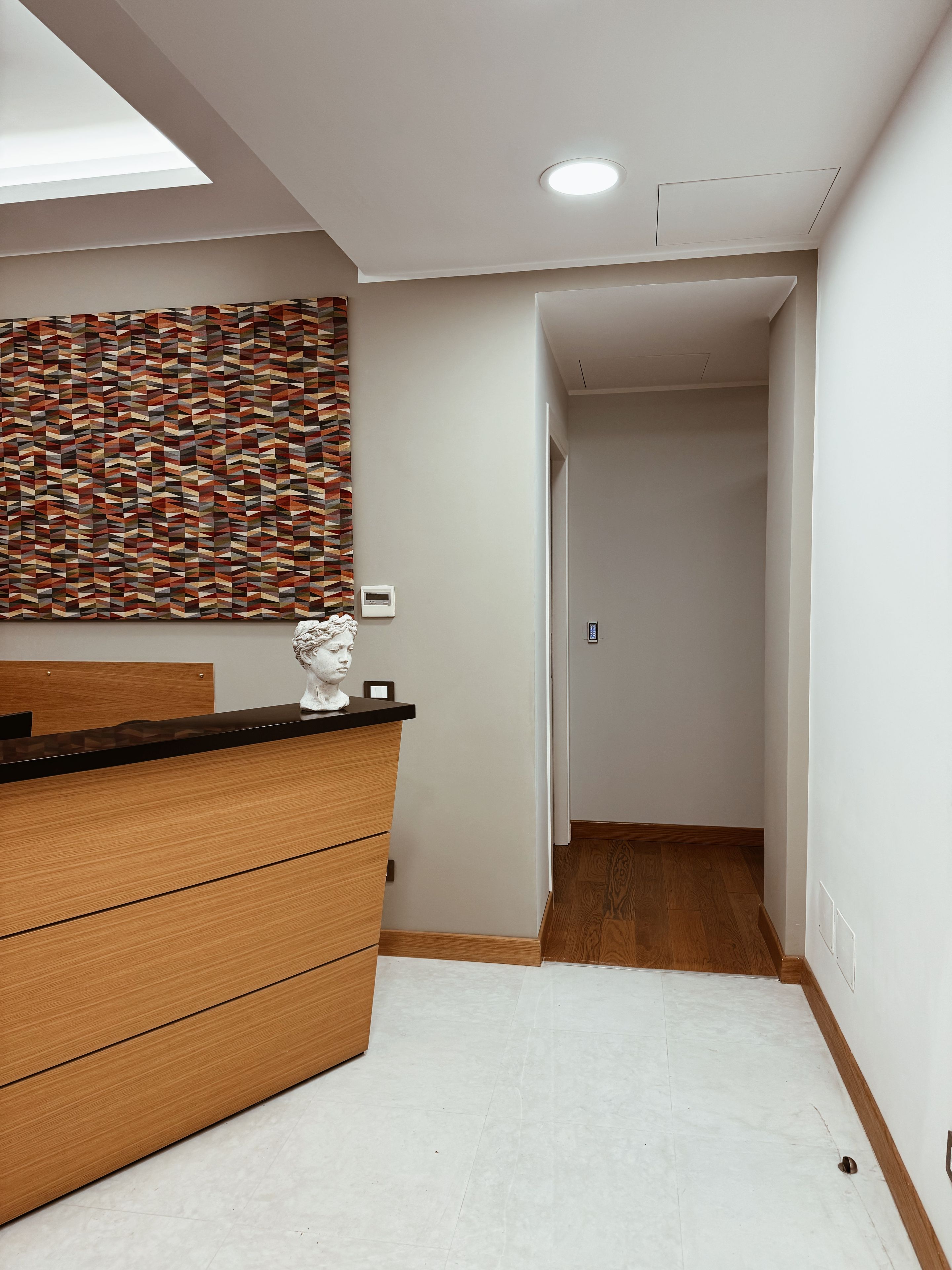 A modern bathroom with a wooden vanity, a geometric patterned wall, and a ceiling light.