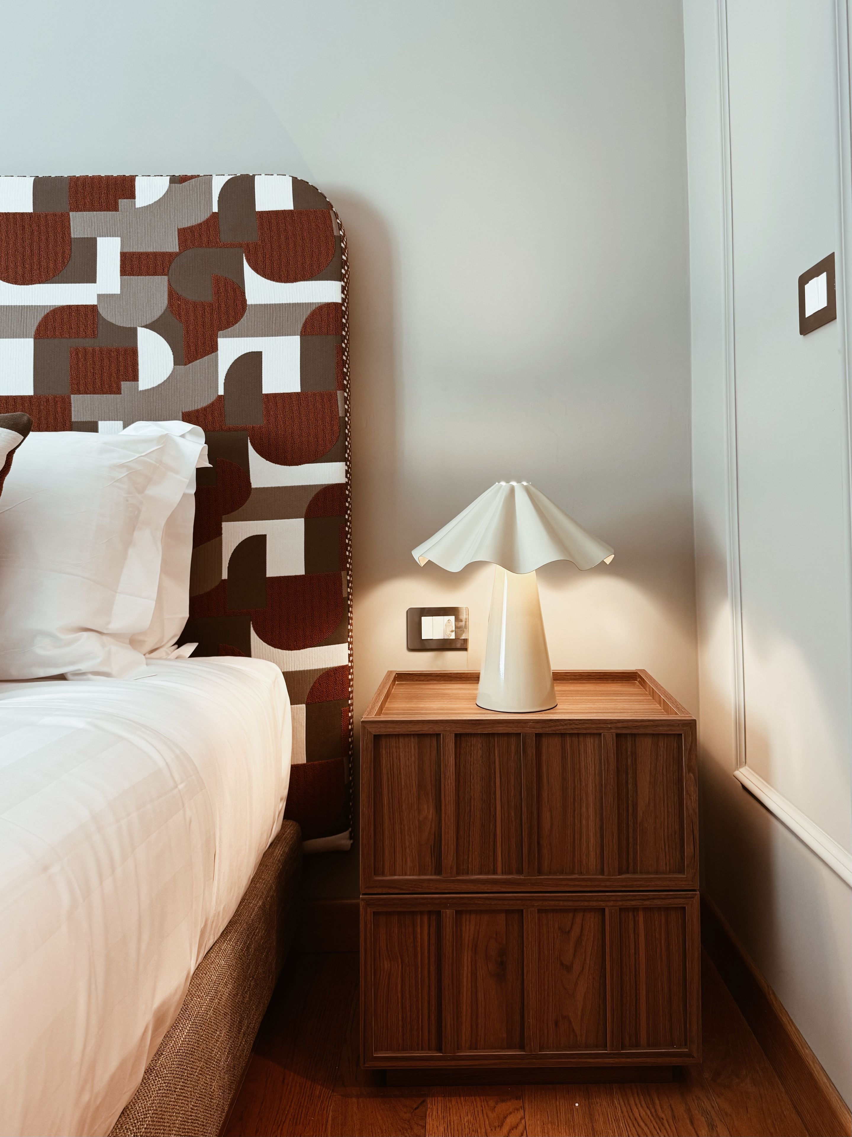 Un dormitorio con cama, una mesita de noche con lámpara y una pared con diseño geométrico.
