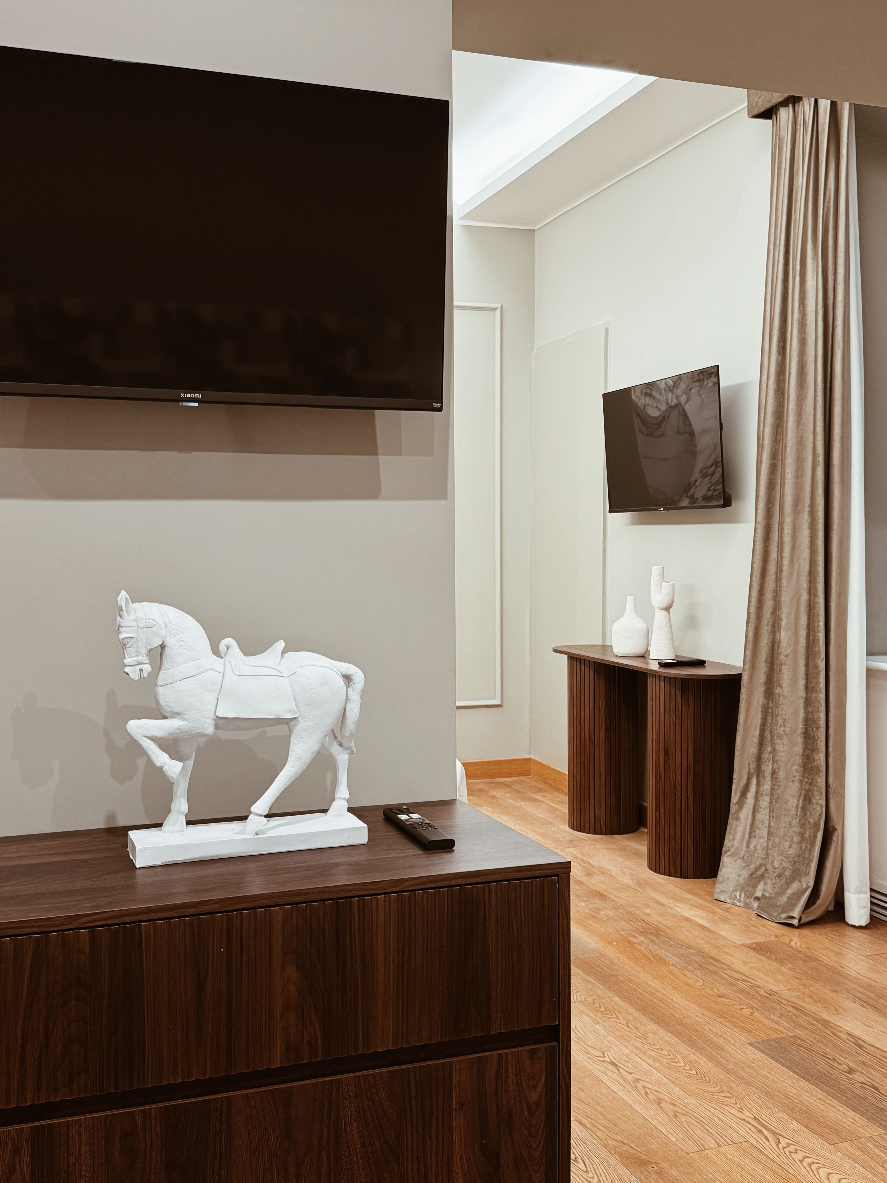 Habitació moderna amb televisió penjada, una escultura de cavall blanc i un armari de fusta.