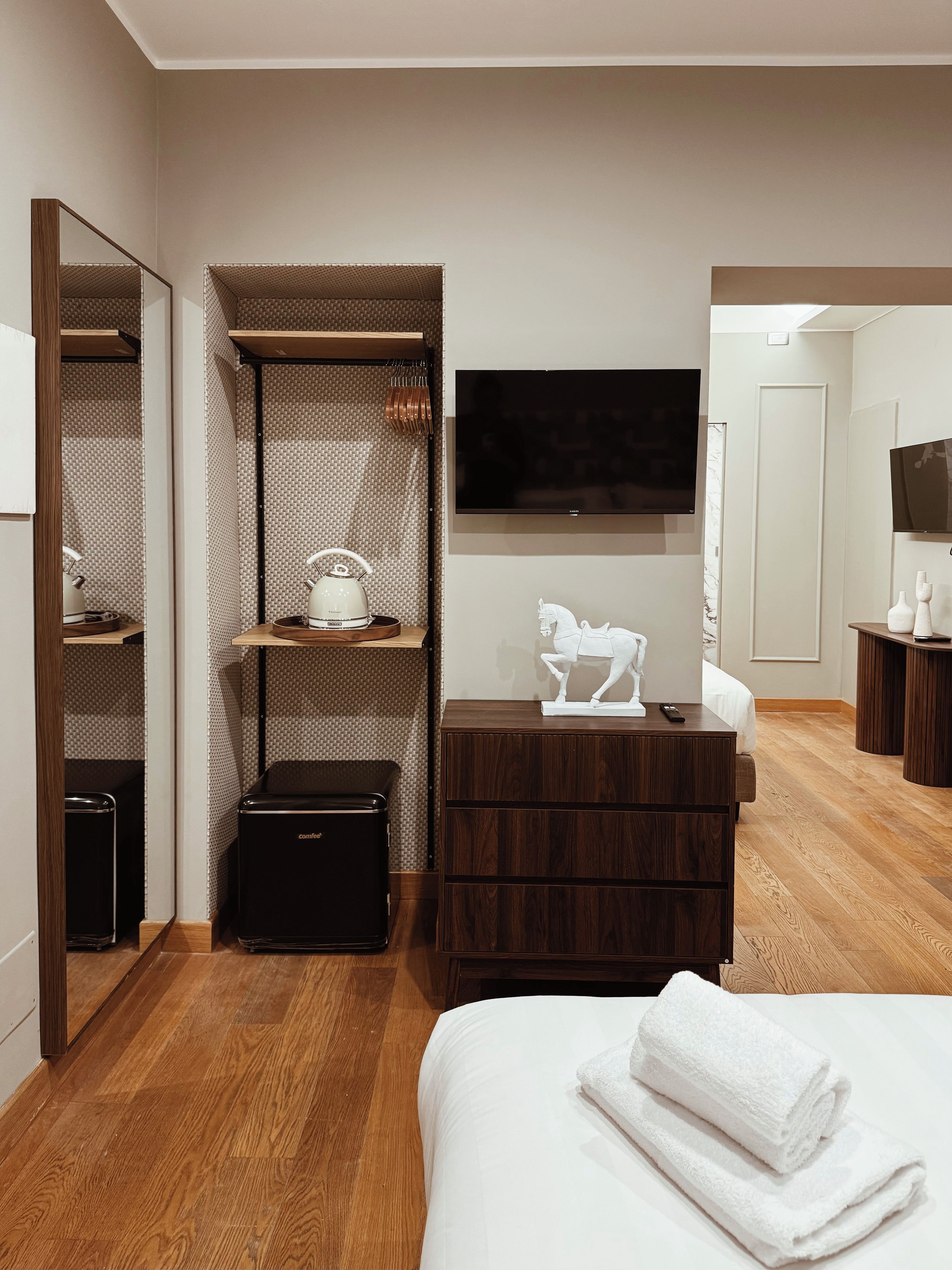 Habitación de hotel con cama, cómoda, televisor, armario y una mesita con tetera.