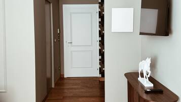 Un pasillo con piso de madera, una puerta blanca, un televisor de pared y una pequeña estatua de un caballo blanco sobre una consola de madera.