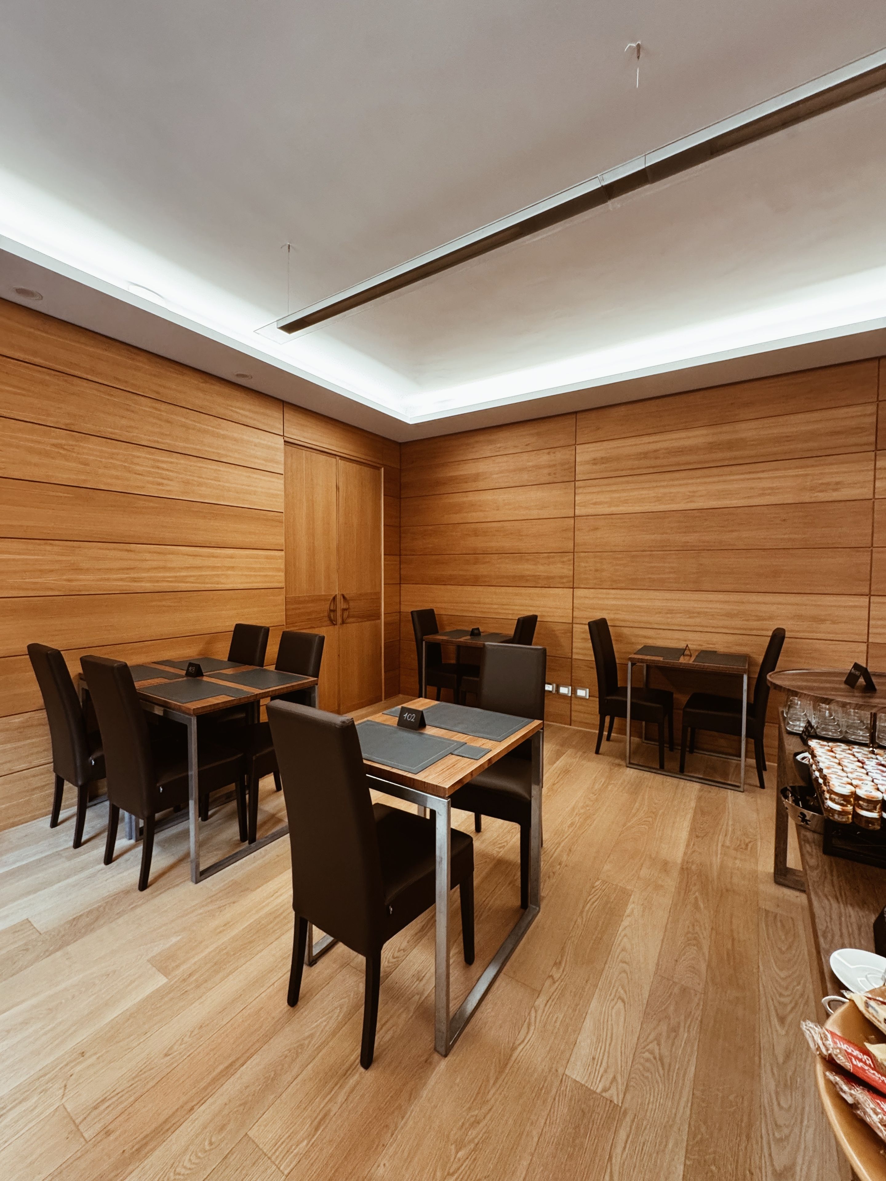 Una sala de conferencias moderna con paredes de paneles de madera, techo alto y tragaluces. Hay varias mesas y sillas dispuestas para reuniones.