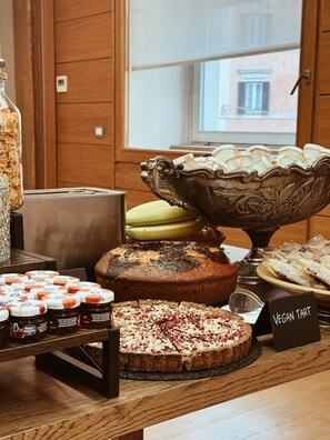A buffet table with various food items including a cake, a bowl of macarons, and jars of spreads. - Residenza Traiana (Rome)