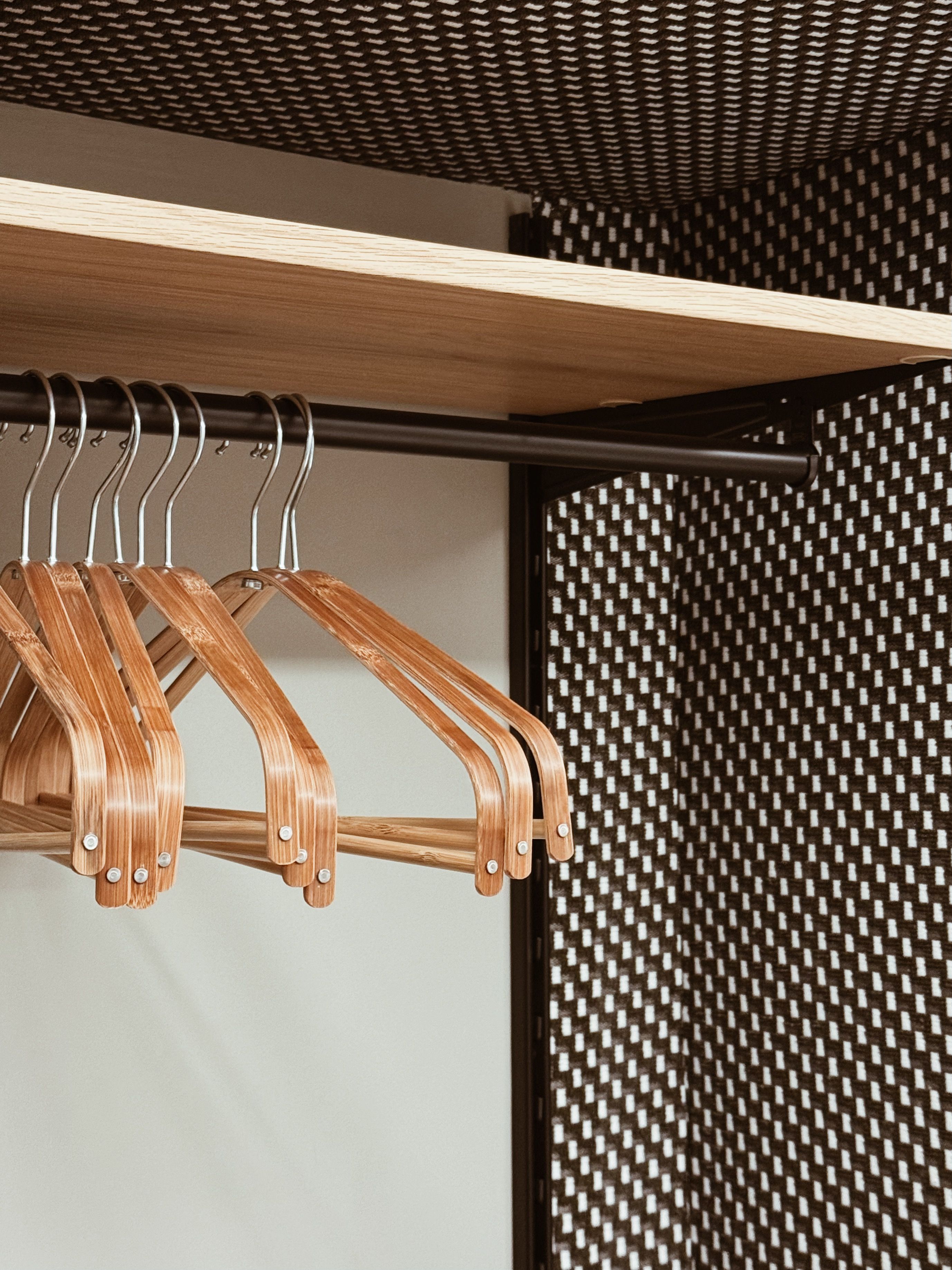 Ein hölzerner Kleiderhaken mit mehreren Kleiderbügeln vor einer Wand mit Karomuster in Schwarz und Weiß.
