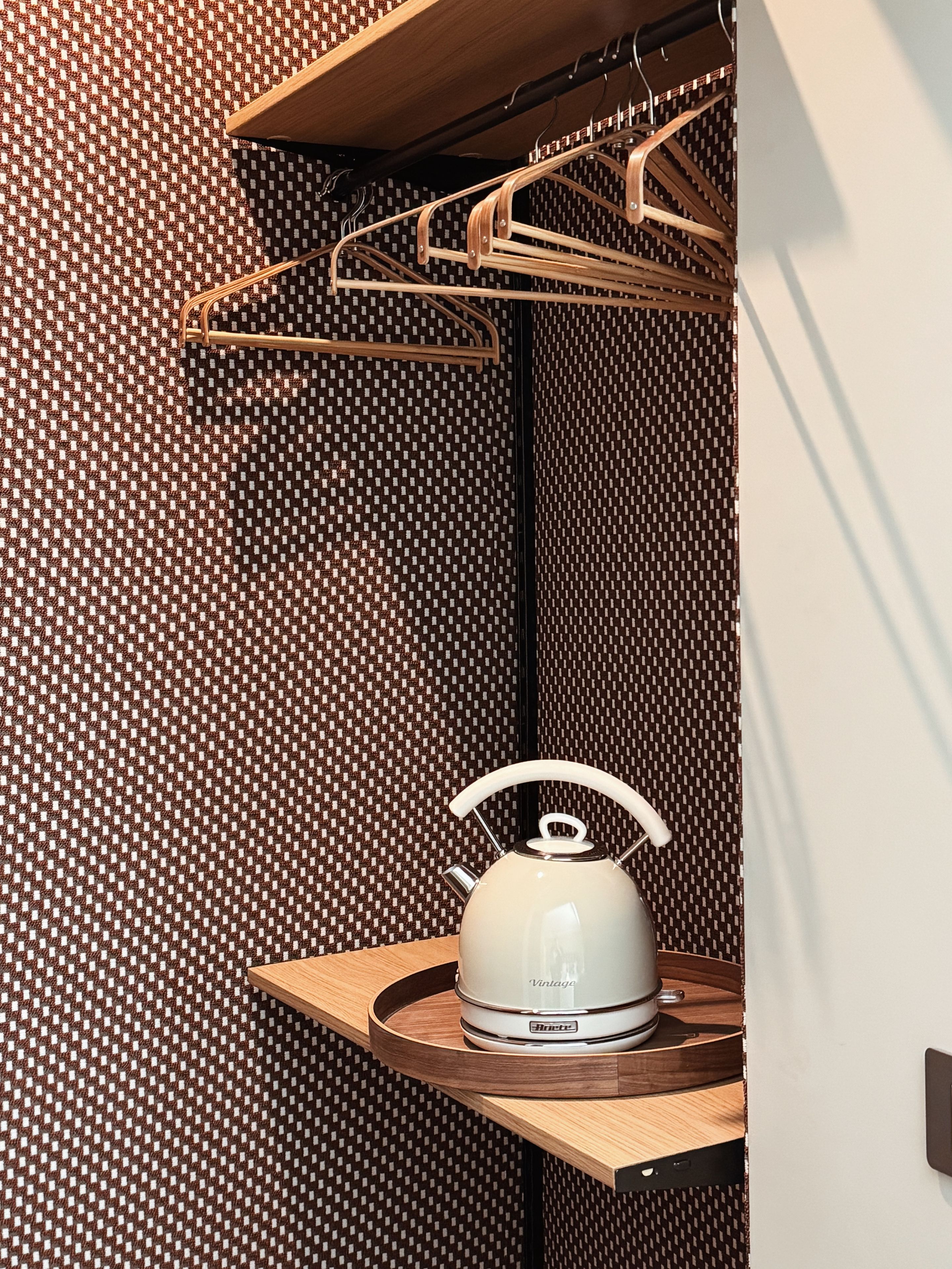 Una cocina compacta con una tetera sobre una encimera de madera, un tendedero encima y una pared con diseño.