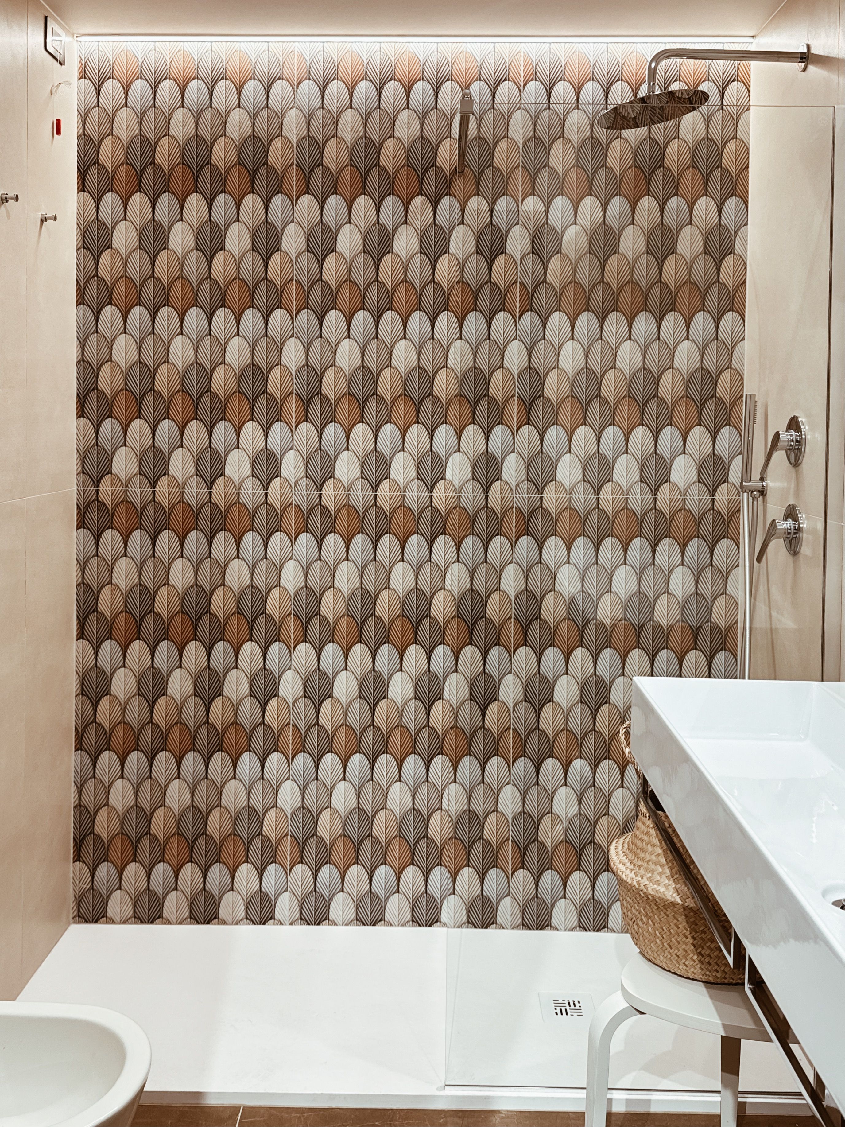 Ein Badezimmer mit einer duschwand mit Muster, einem weißen Waschbecken und einer weißen Toilette.