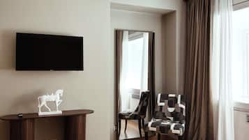 A hotel room with a bed, a flat-screen TV mounted on the wall, a desk with a statue, a chair, and a window with curtains.