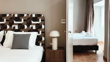 Una habitación de hotel con una cama, una mesita de noche, una lámpara y una puerta abierta que da a otra habitación.