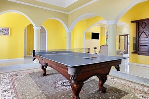 A ping pong table in a room with yellow walls and white arches. - Hospitality Expert VSV TF 3BR Chef Pool  (Montego Bay)