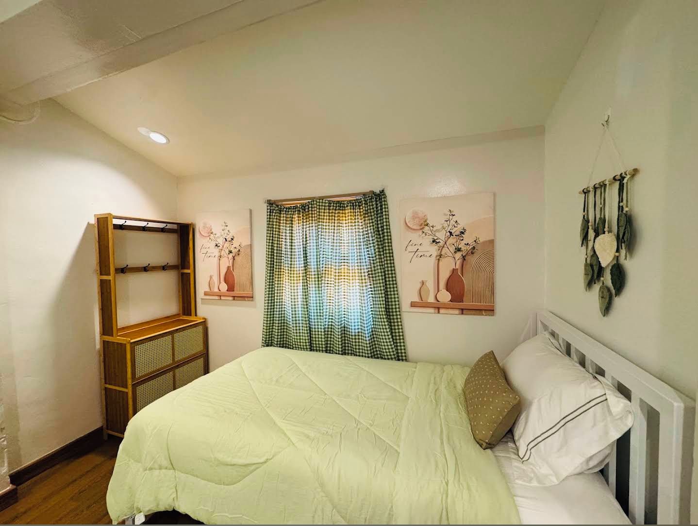 A bedroom with a bed, a wooden shelf unit, a checkered curtain, and wall art.