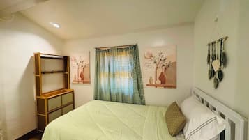 A bedroom with a bed, a wooden shelf unit, a checkered curtain, and wall art.