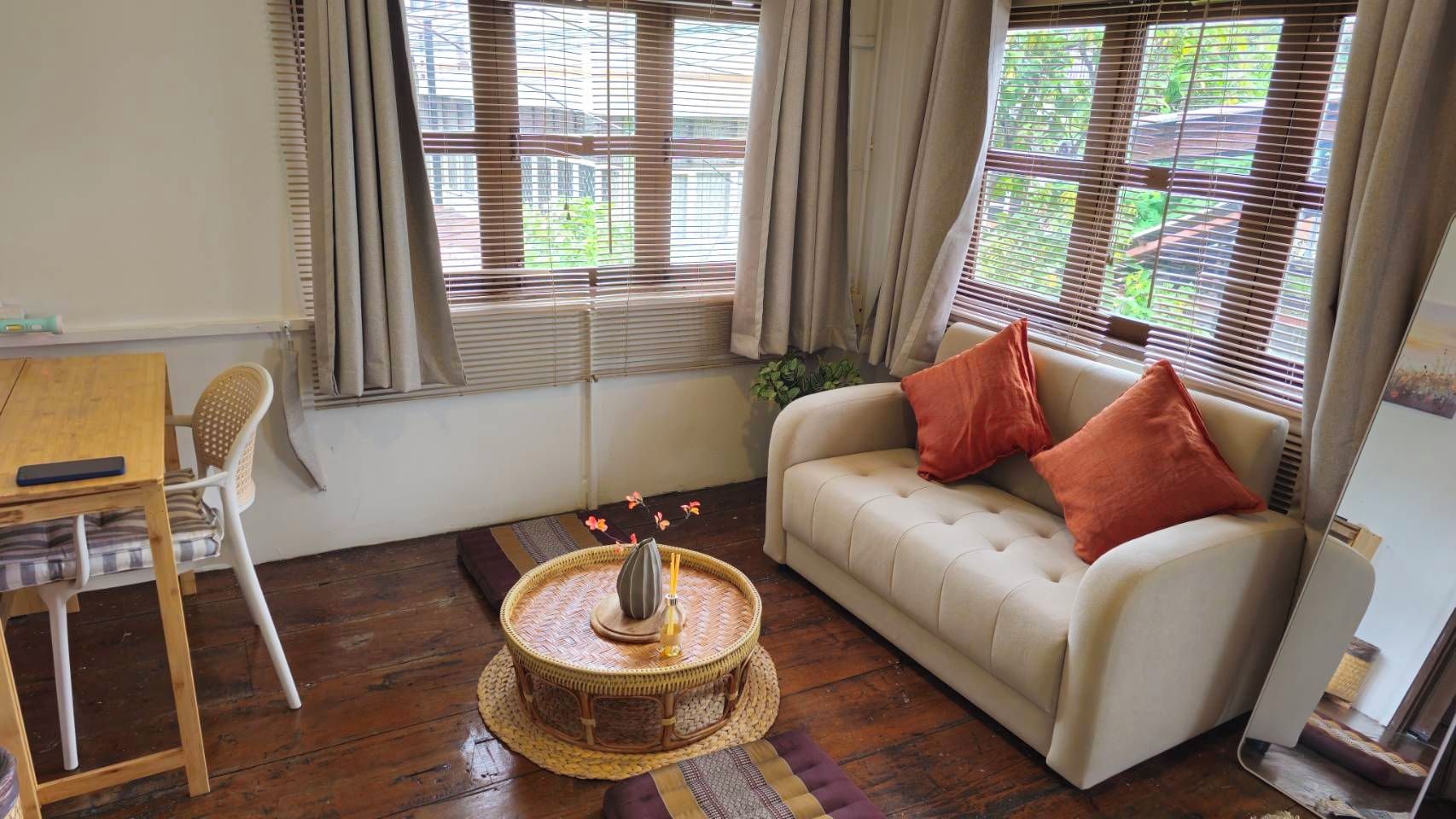 Una habitación con un sofá, una mesa redonda tejida, una silla y una pequeña mesa con un jarrón.
