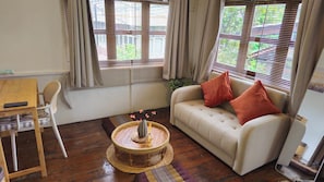 A room with a sofa, a round woven table, a chair, and a small table with a vase. - Charming Home Chiang Mai (Chiang Mai)
