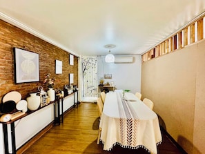 A dining area with a long table, chairs, a wooden floor, a brick wall, and a ceiling fan. - Charming Home Chiang Mai (Chiang Mai)