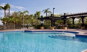 Ein Schwimmbecken mit einer Holzpergola und Palmen im Hintergrund.