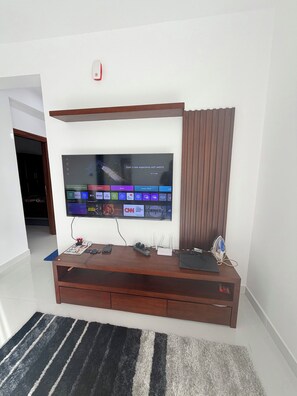 A flat-screen TV mounted on a wooden entertainment unit with a remote control and a smartphone on it. - Spacious Sea View Apartment  3 Bedrooms  2 Bathrooms (Colombo)
