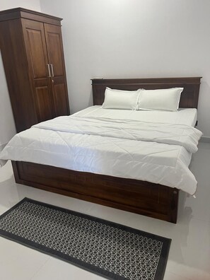 A bedroom with a bed, white bedding, a wooden wardrobe, and a patterned mat.