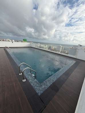 A rooftop swimming pool with a view of the city skyline and the sea.