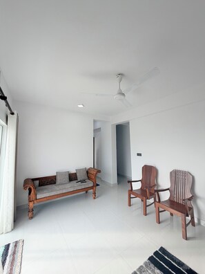 A living room with a sofa, two wooden chairs, a ceiling fan, and a door.