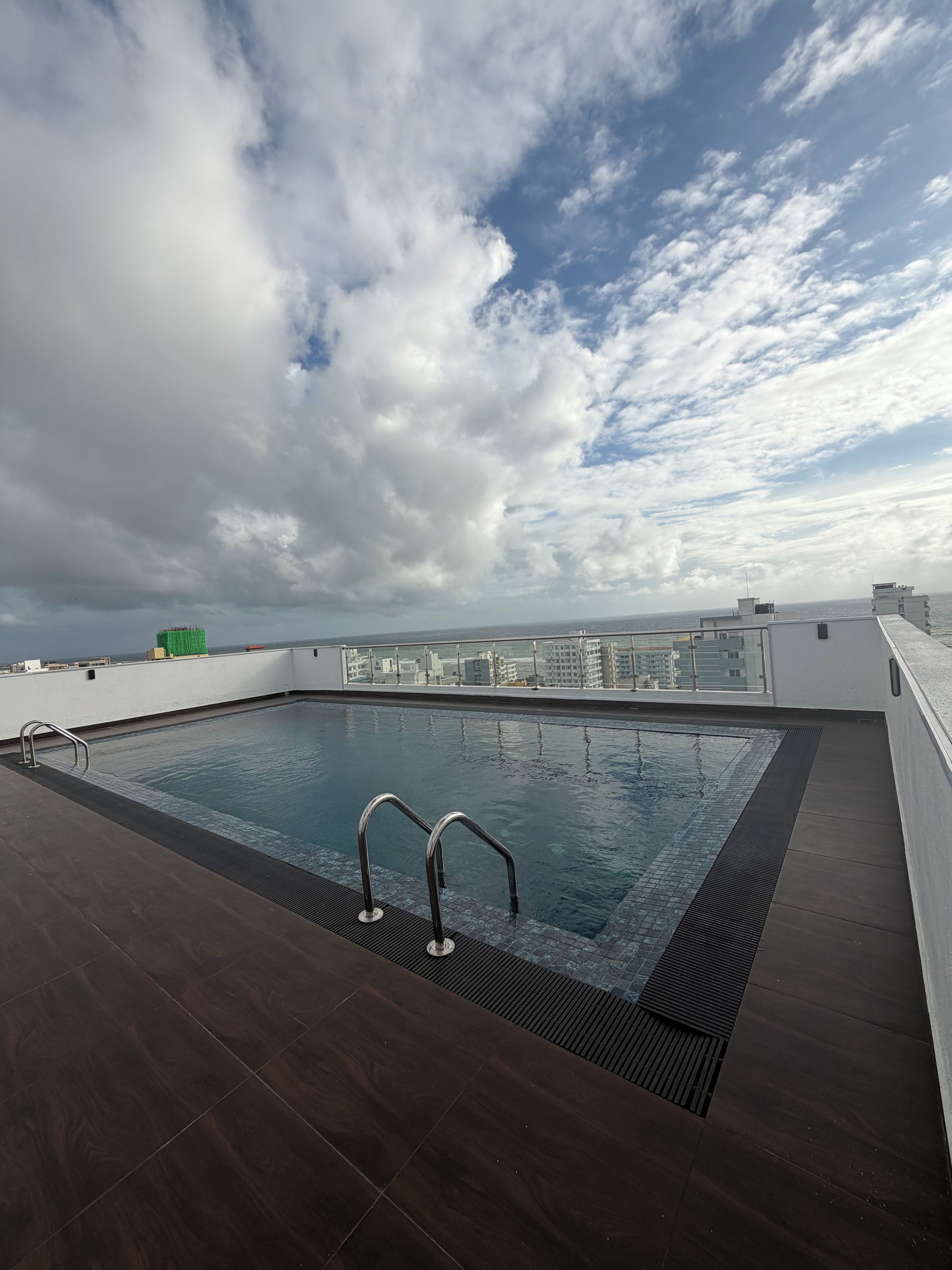A rooftop swimming pool with a view of the city skyline and clouds in the sky.