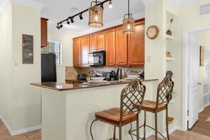 Une cuisine avec des meubles en bois, un îlot central, des tabourets de bar et des luminaires suspendus.
