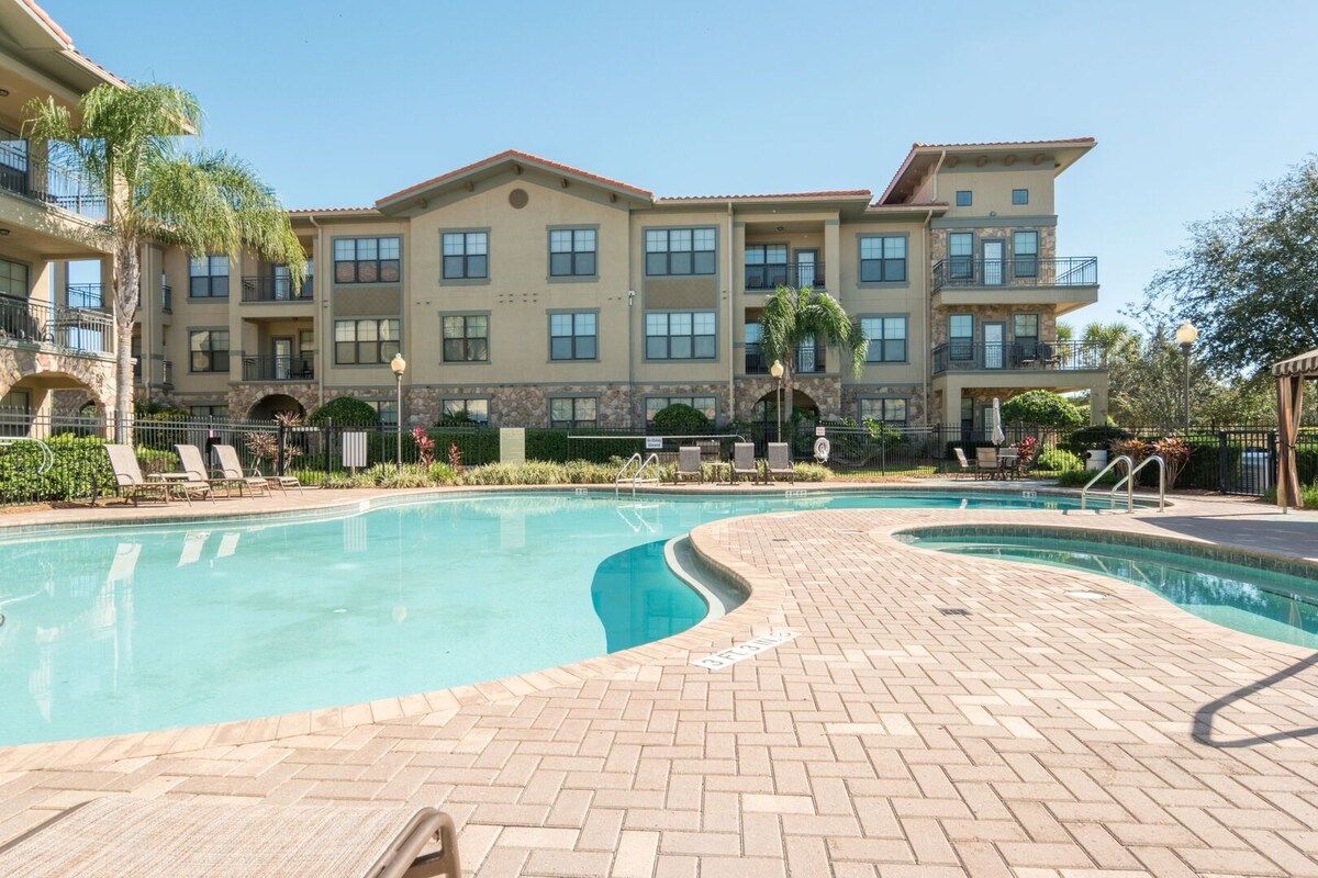 A swimming pool with a brick deck, surrounded by lounge chairs and palm trees.