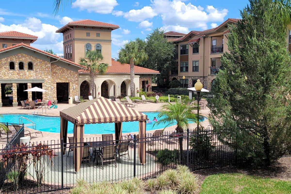 A resort with a swimming pool, outdoor seating, and a stone building with arches.